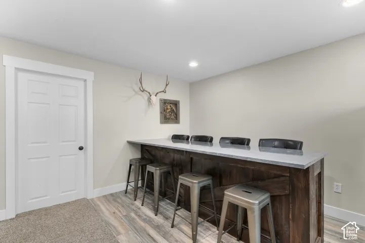 Built-in bar with a light-toned countertop, wood-finish base, recessed lighting, and wood-finish flooring
