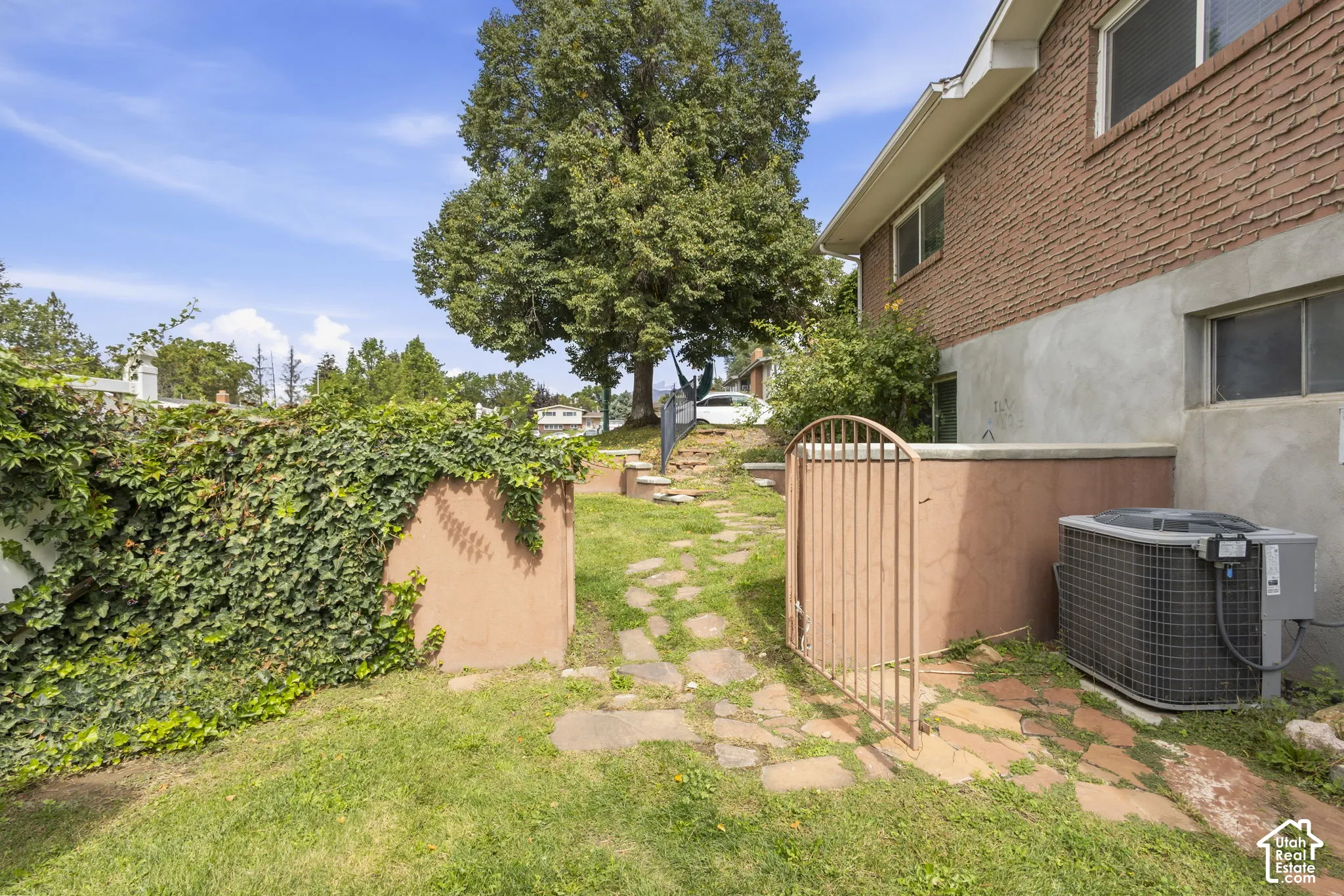 Brick exterior with an established tree, terraced landscaping, a stone pathway, and a metal gate
