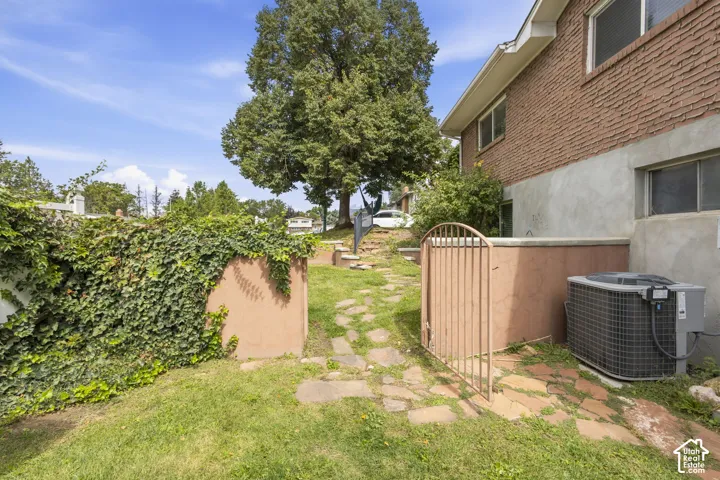Brick exterior with an established tree, terraced landscaping, a stone pathway, and a metal gate