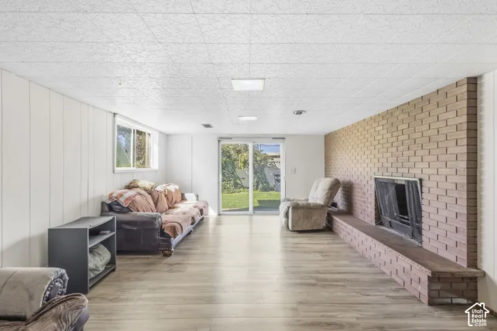 Wood-finish flooring, brick-faced fireplace, white paneled walls, and sliding glass door with independent access directly from private backyard