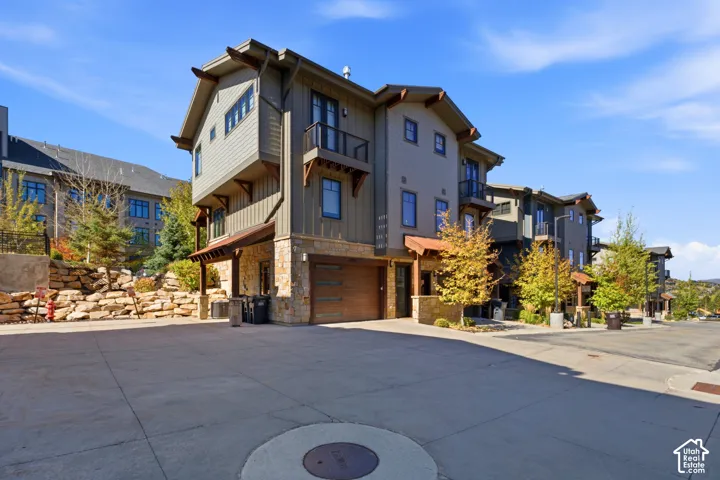 Multi-story exterior featuring stone accents, a wood-finish garage door, prominent eaves, and multiple balconies