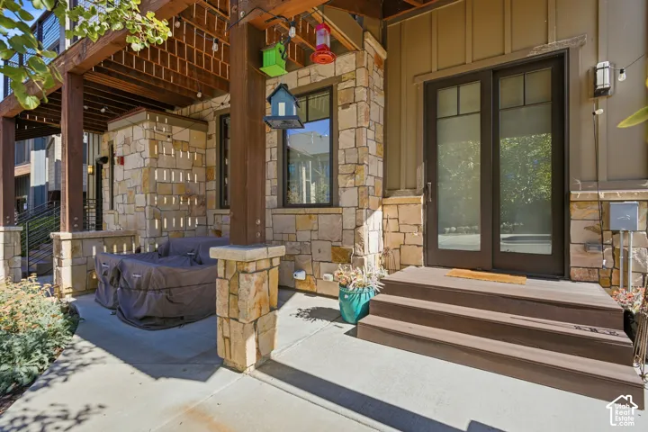 Stone veneer accents, multi-level patio, wood-finish stairs, dark-framed glass doors, and a wood pergola