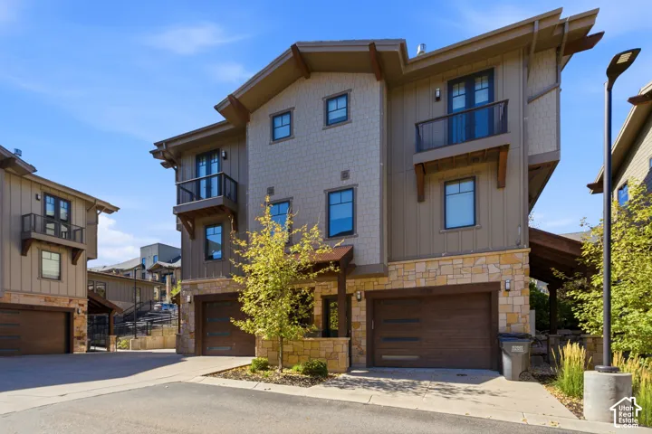 Multi-level residence featuring stone and siding exterior, multiple balconies with dark railings, integrated two-car garage, and a covered entry