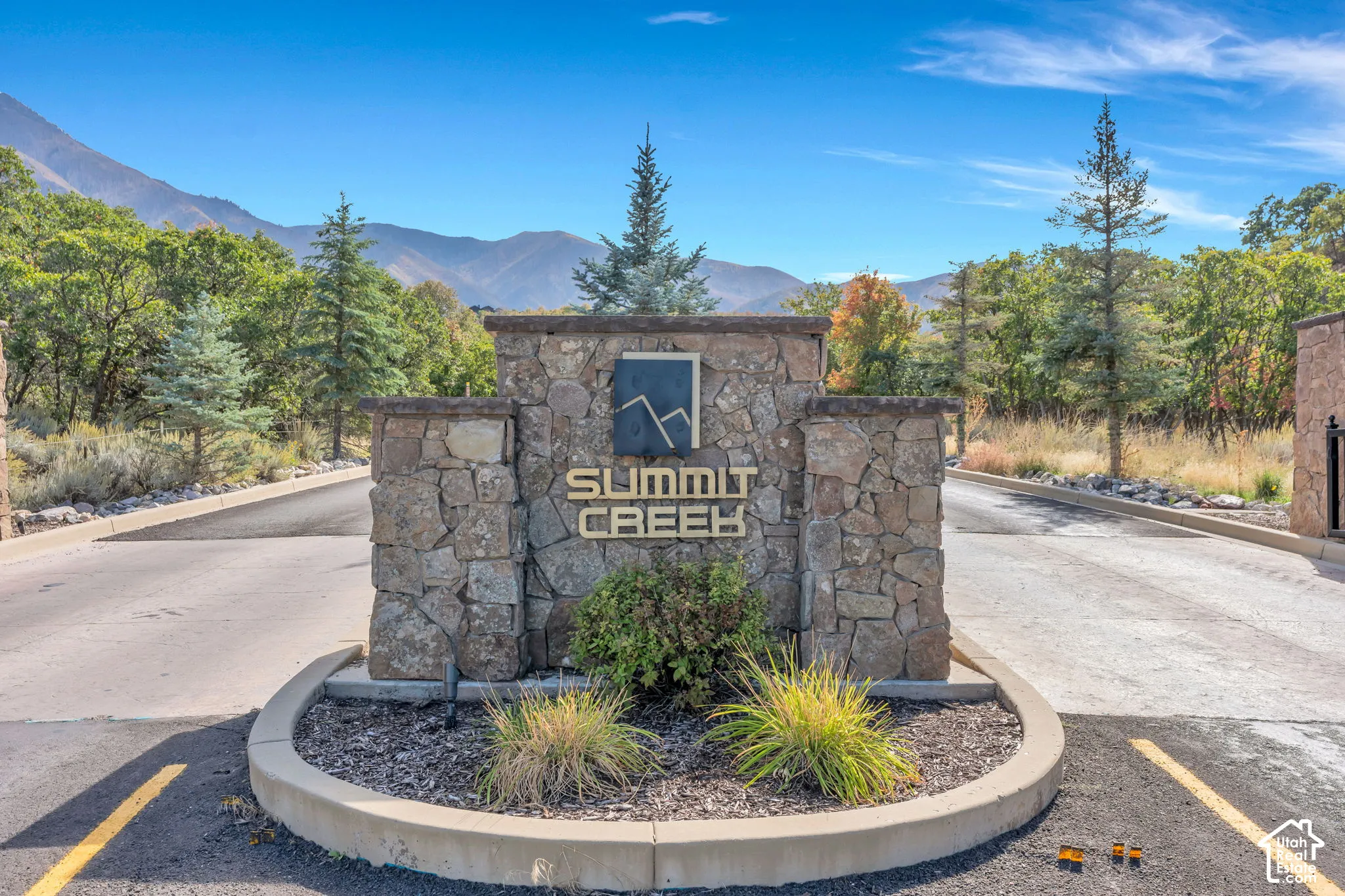 Stone monument sign featuring the "Summit Creek" nameplate, surrounded by natural landscaping, and backed by mature trees and mountains