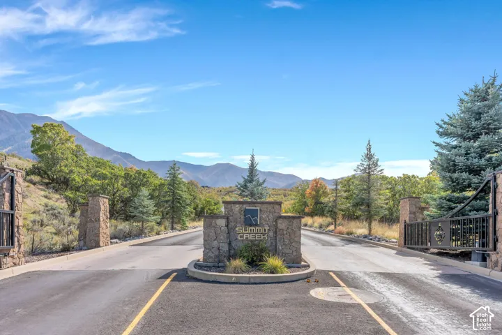 Stone-clad entry pillars with wrought iron gates, a central stone monument, and paved roadway with natural landscaping