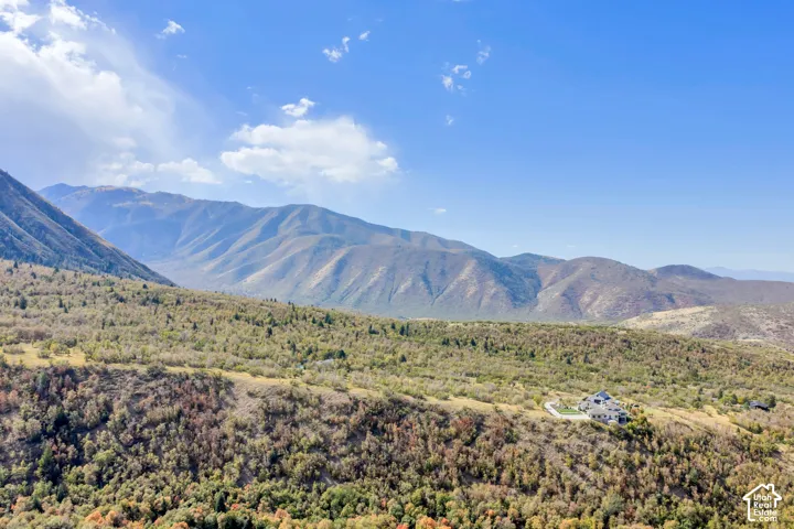 Expansive mountainous terrain with a residential structure, surrounding natural foliage, and varied topography