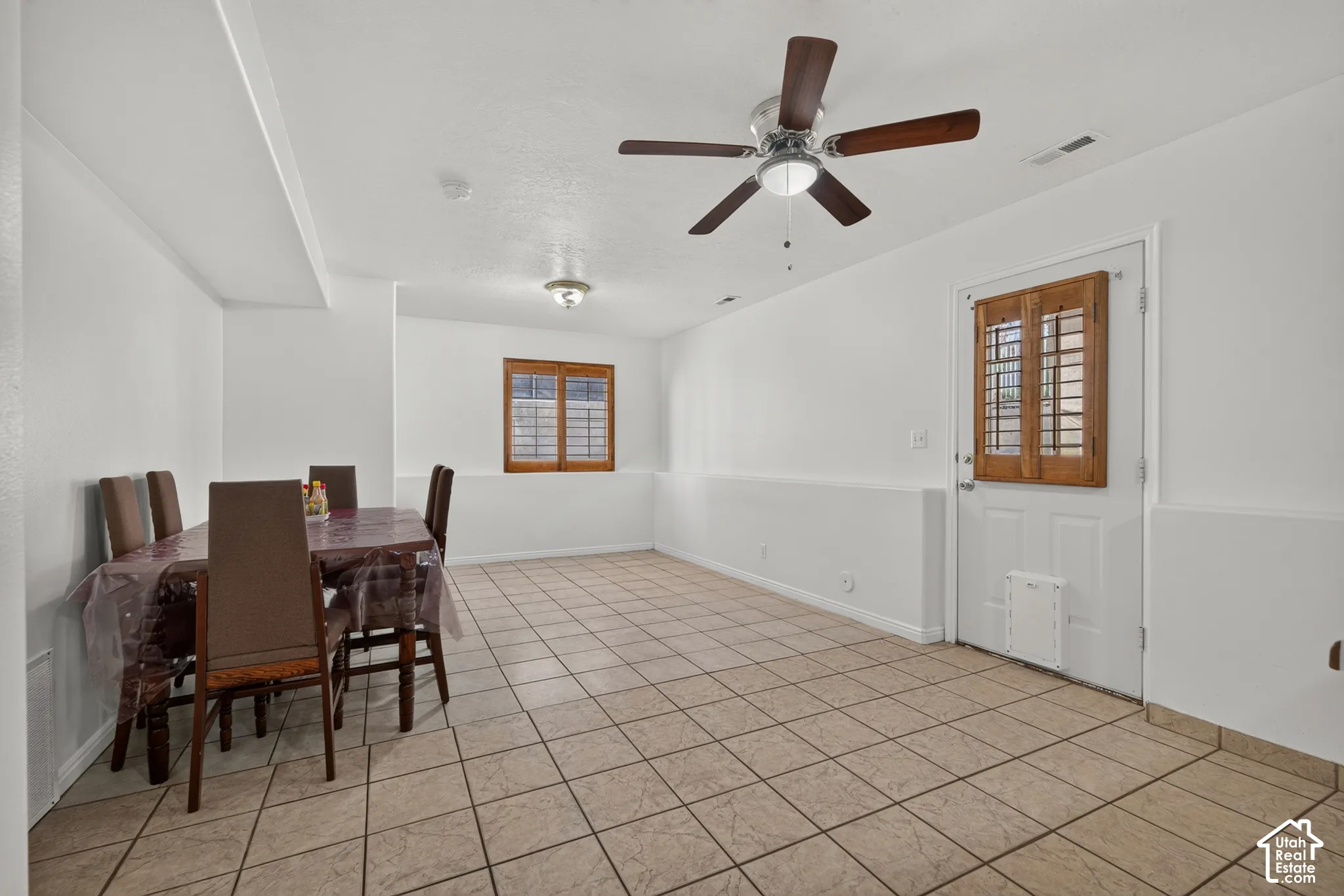 Tile flooring throughout, white walls, wood-finish window shutters, and a ceiling fan with integrated lighting