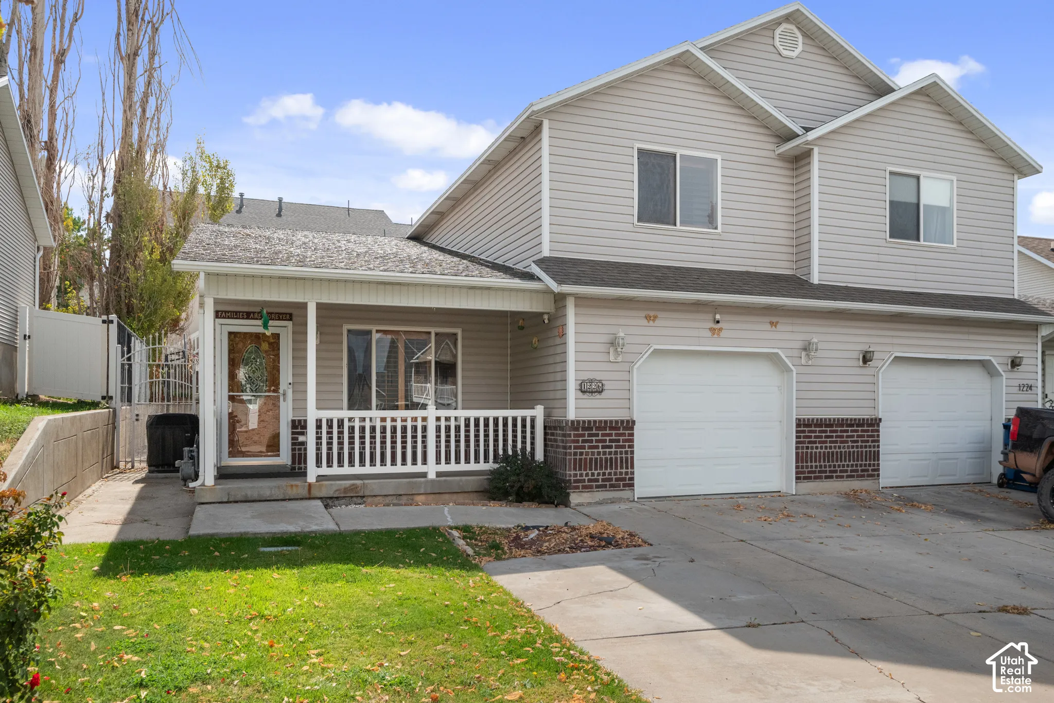 Two-story exterior with light-colored siding, brick detailing, covered front porch with white railing, and a two-car garage