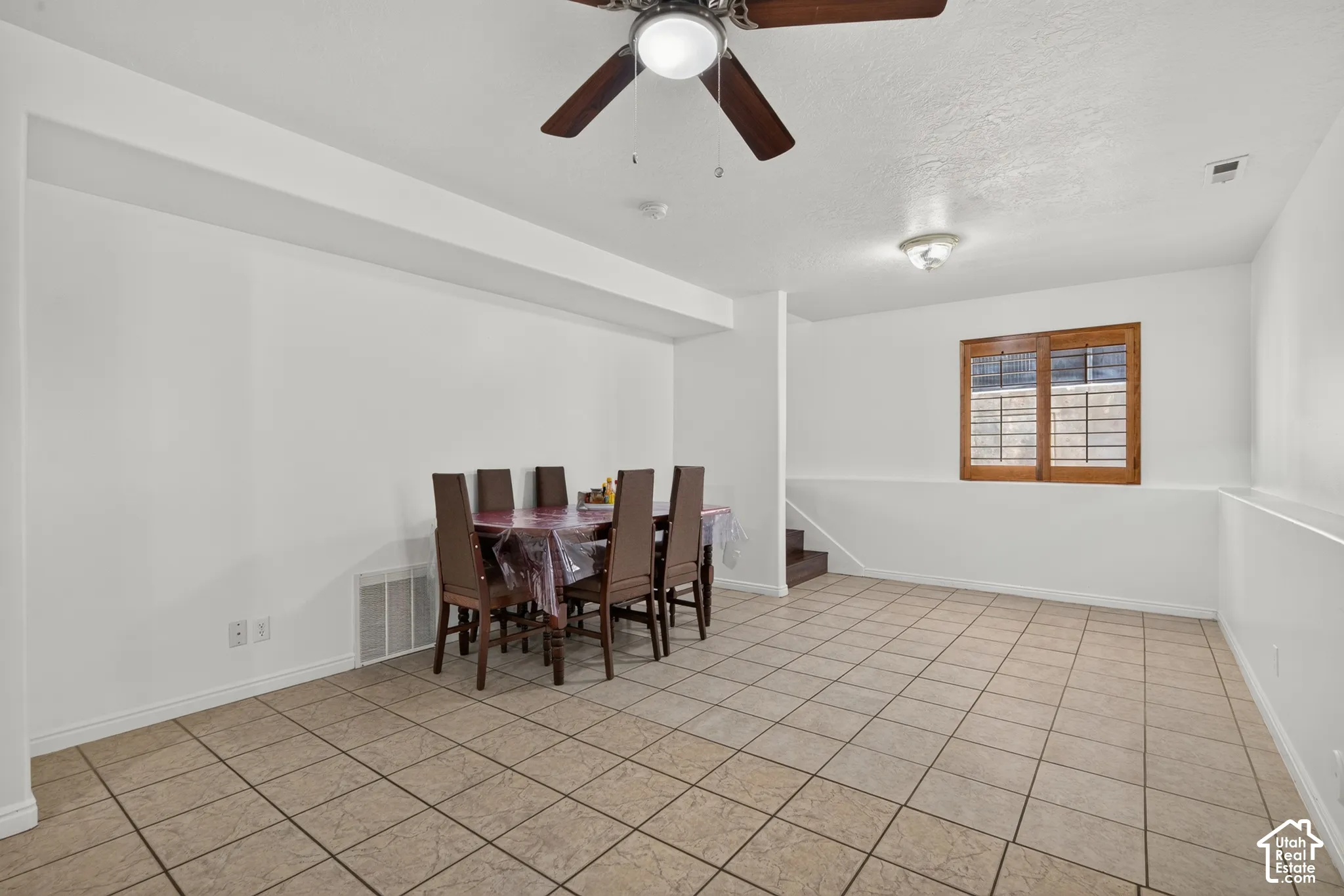 Recessed ceiling with wood-finish ceiling fan, square tile flooring, wood-framed window with integrated blinds, and built-in steps