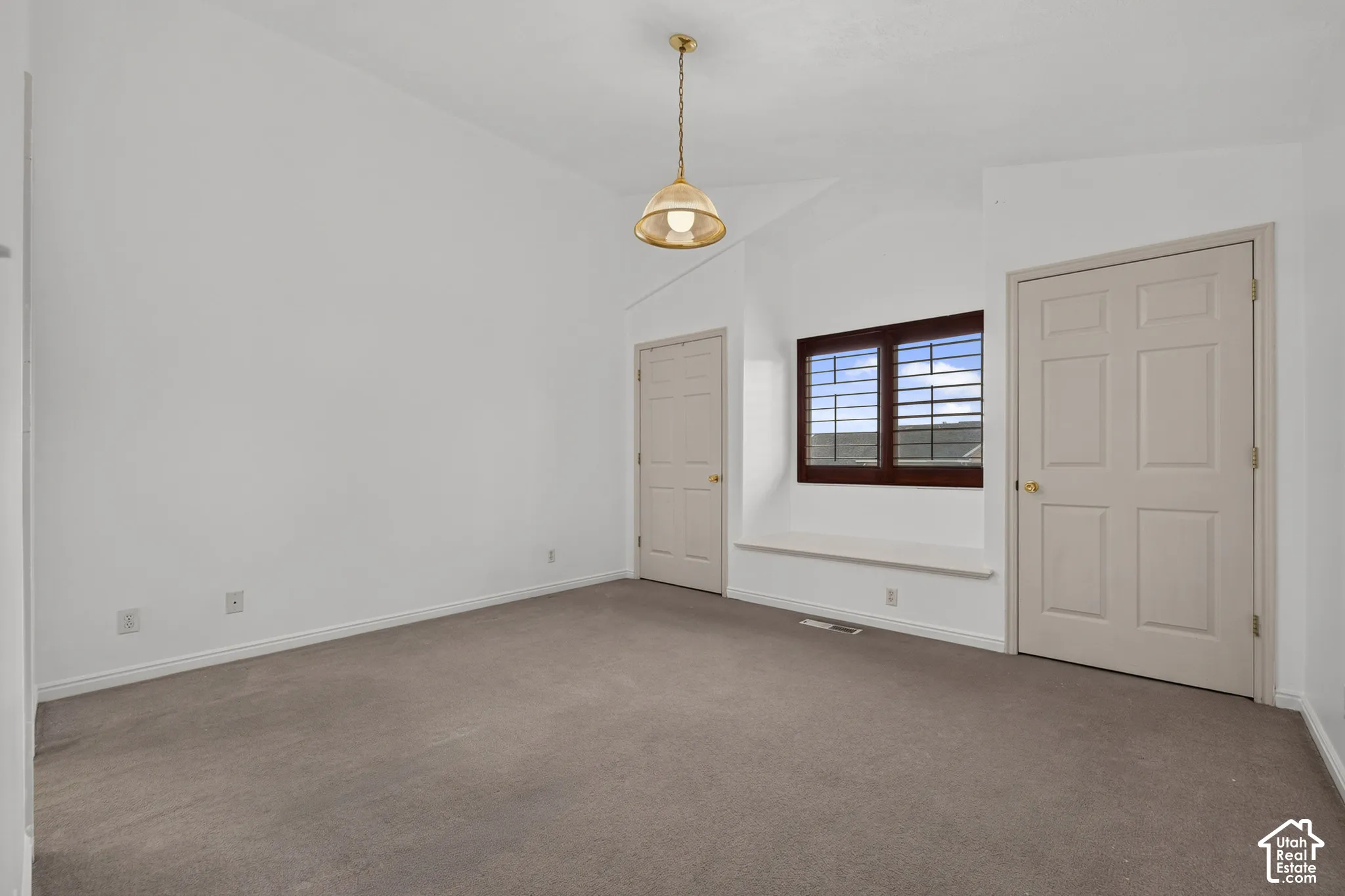 Vaulted ceiling with a suspended light fixture, a window with plantation shutters, a built-in window bench, and neutral carpeting