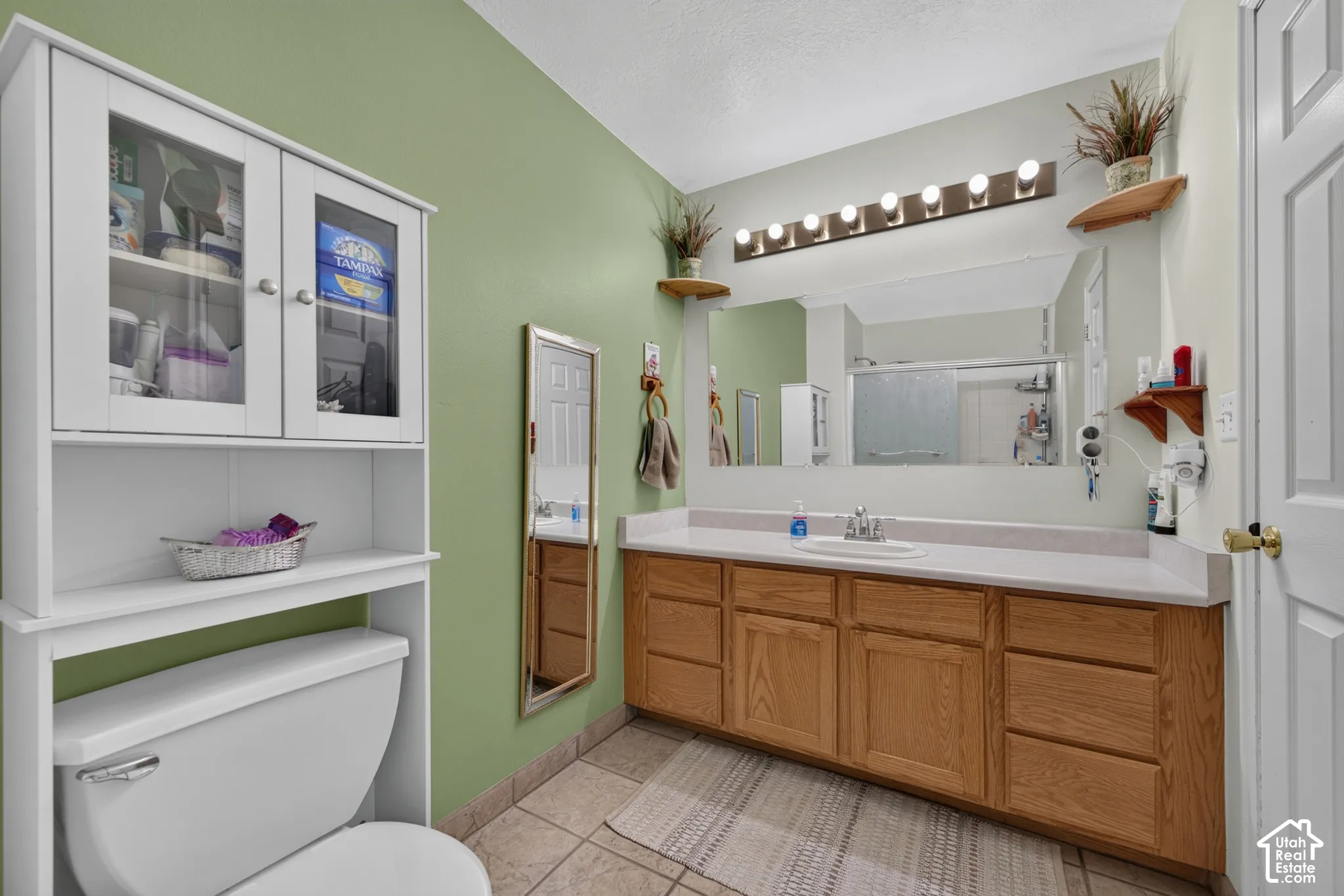 Dual-tone wall treatment with a large vanity mirror, a wood-finish vanity with ample storage, a white over-the-toilet cabinet with glass-front doors, and tile flooring
