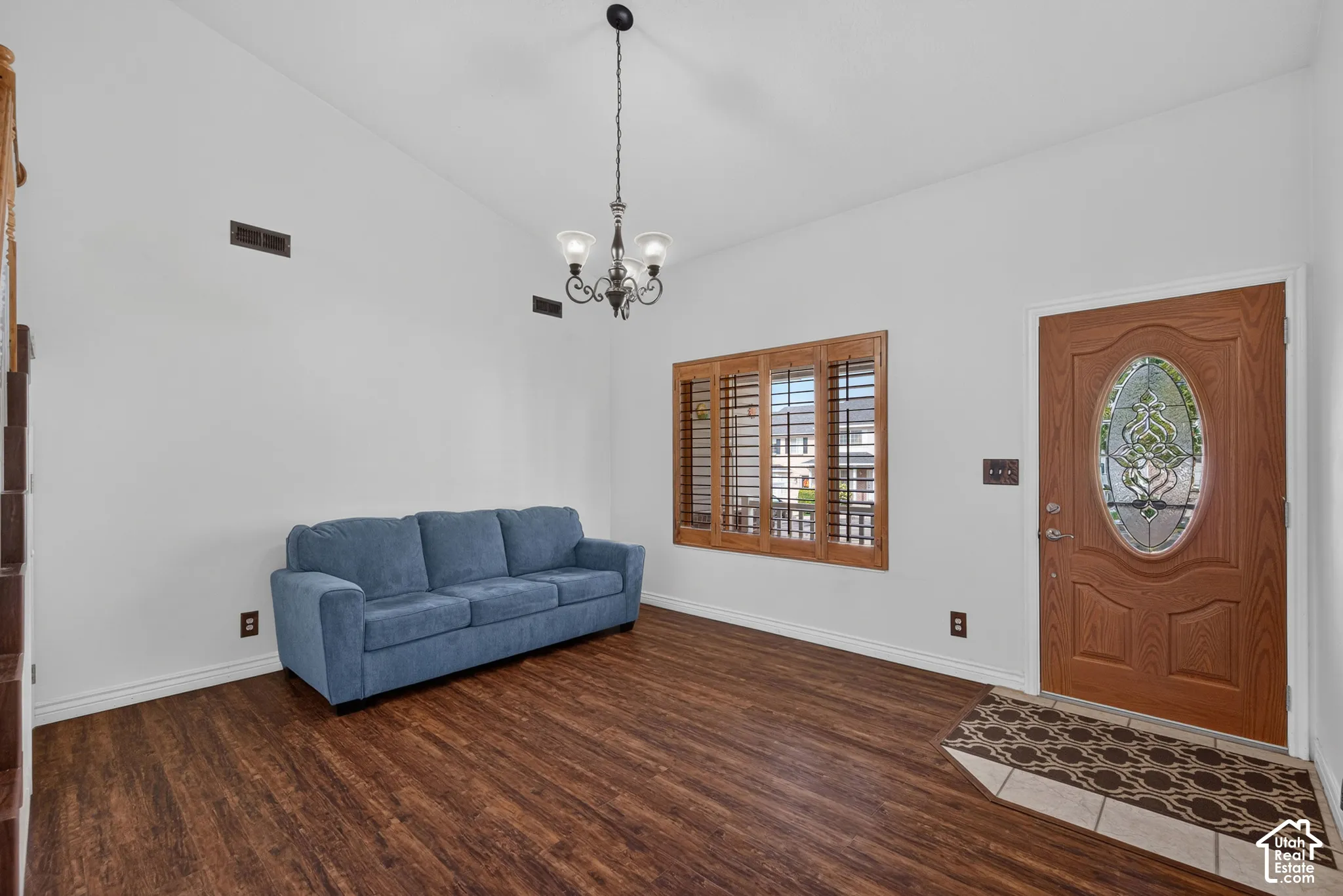 Vaulted ceiling with a chandelier, wood-finish flooring, and a paneled entry door with an oval leaded glass insert