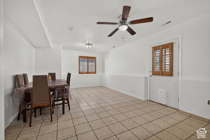 Tile flooring throughout, white walls, wood-finish window shutters, and a ceiling fan with integrated lighting