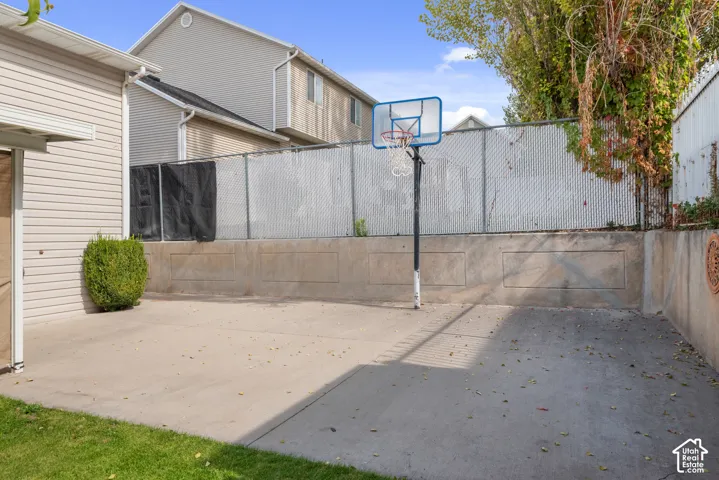Paved outdoor space featuring a basketball hoop, chain-link fencing, and a concrete retaining wall