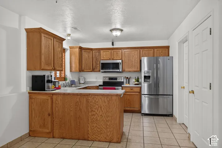 Wood cabinetry with crown molding, stainless steel appliances, light countertops, tiled flooring, and pantry doors
