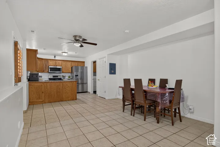 Open-concept kitchen and dining area featuring light-toned tile flooring, wood cabinetry, and stainless steel appliances