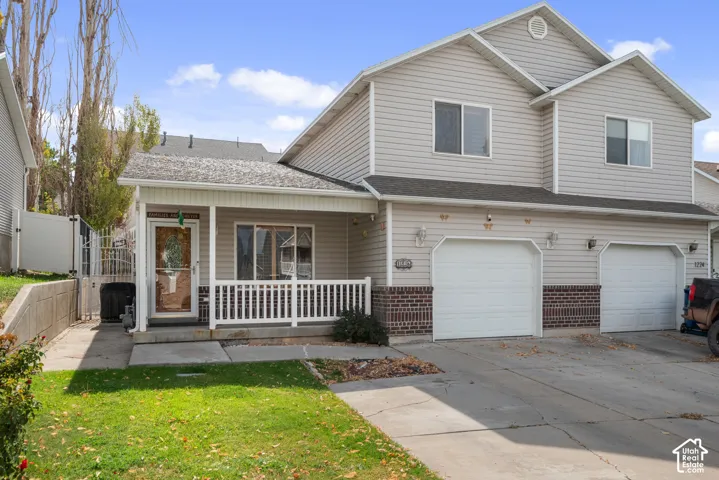 Two-story exterior with light-colored siding, brick detailing, covered front porch with white railing, and a two-car garage
