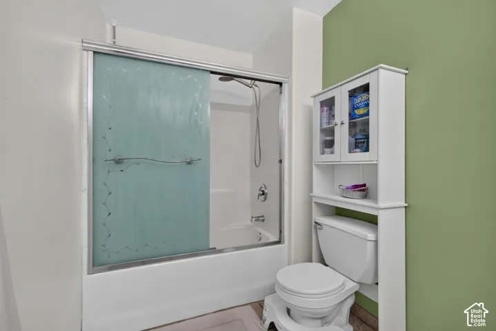 Bathtub with sliding glass enclosure, shower head, toilet, and built-in storage cabinet