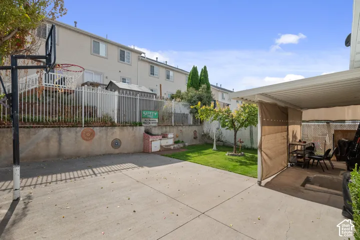 Expansive concrete patio with a covered outdoor area, featuring a grassy lawn and established trees
