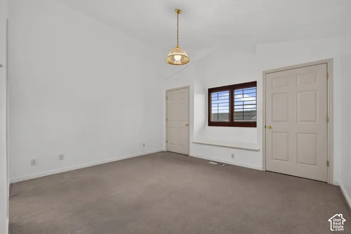 Vaulted ceiling with a suspended light fixture, a window with plantation shutters, a built-in window bench, and neutral carpeting