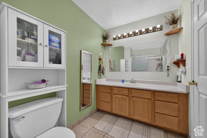 Dual-tone wall treatment with a large vanity mirror, a wood-finish vanity with ample storage, a white over-the-toilet cabinet with glass-front doors, and tile flooring