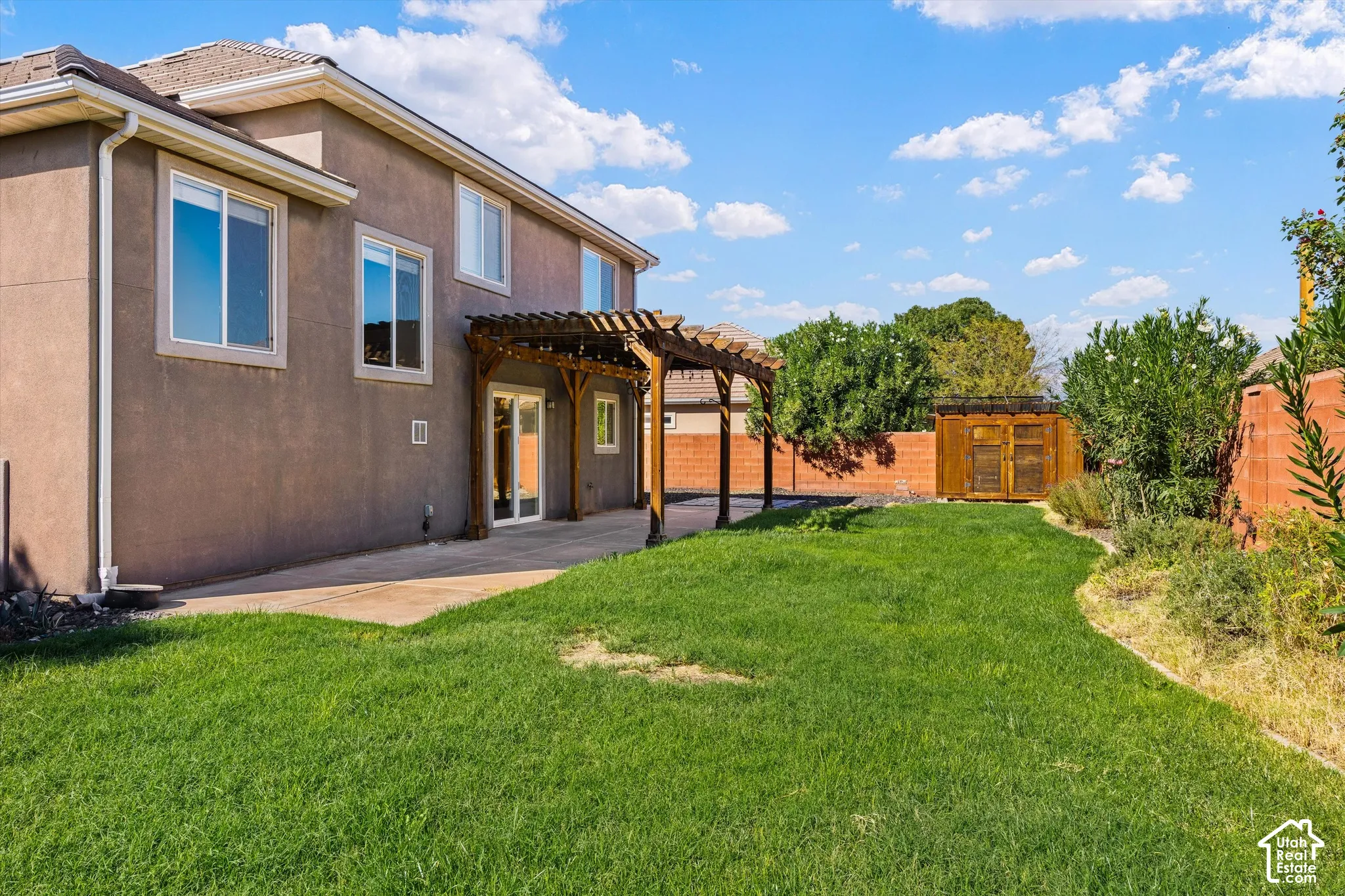 Expansive lawn with a concrete patio, wood pergola, and wood storage shed