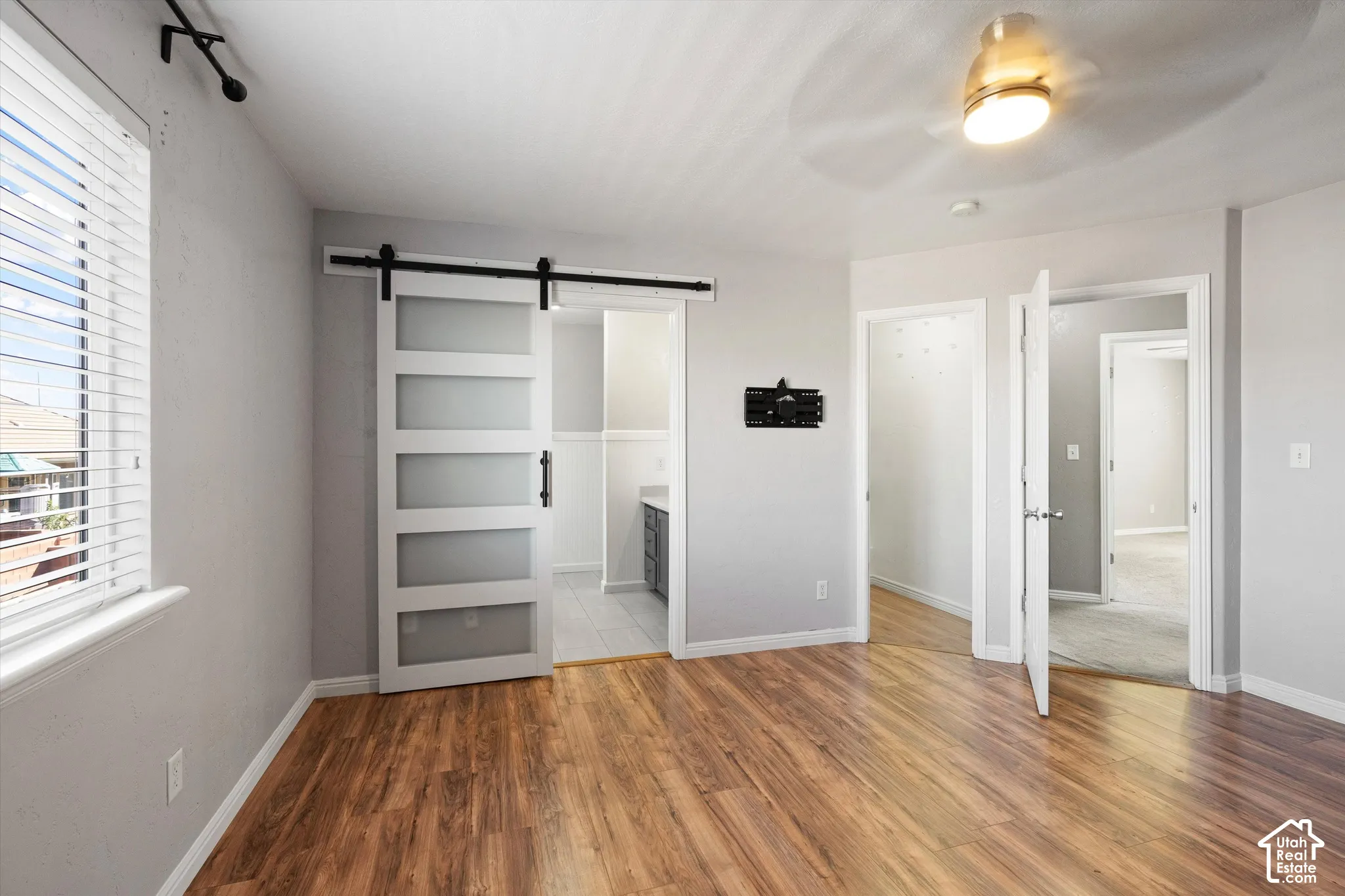Wood-finish flooring, white window blinds, modern barn door with frosted panels, ceiling fan with integrated light, and multiple doorways