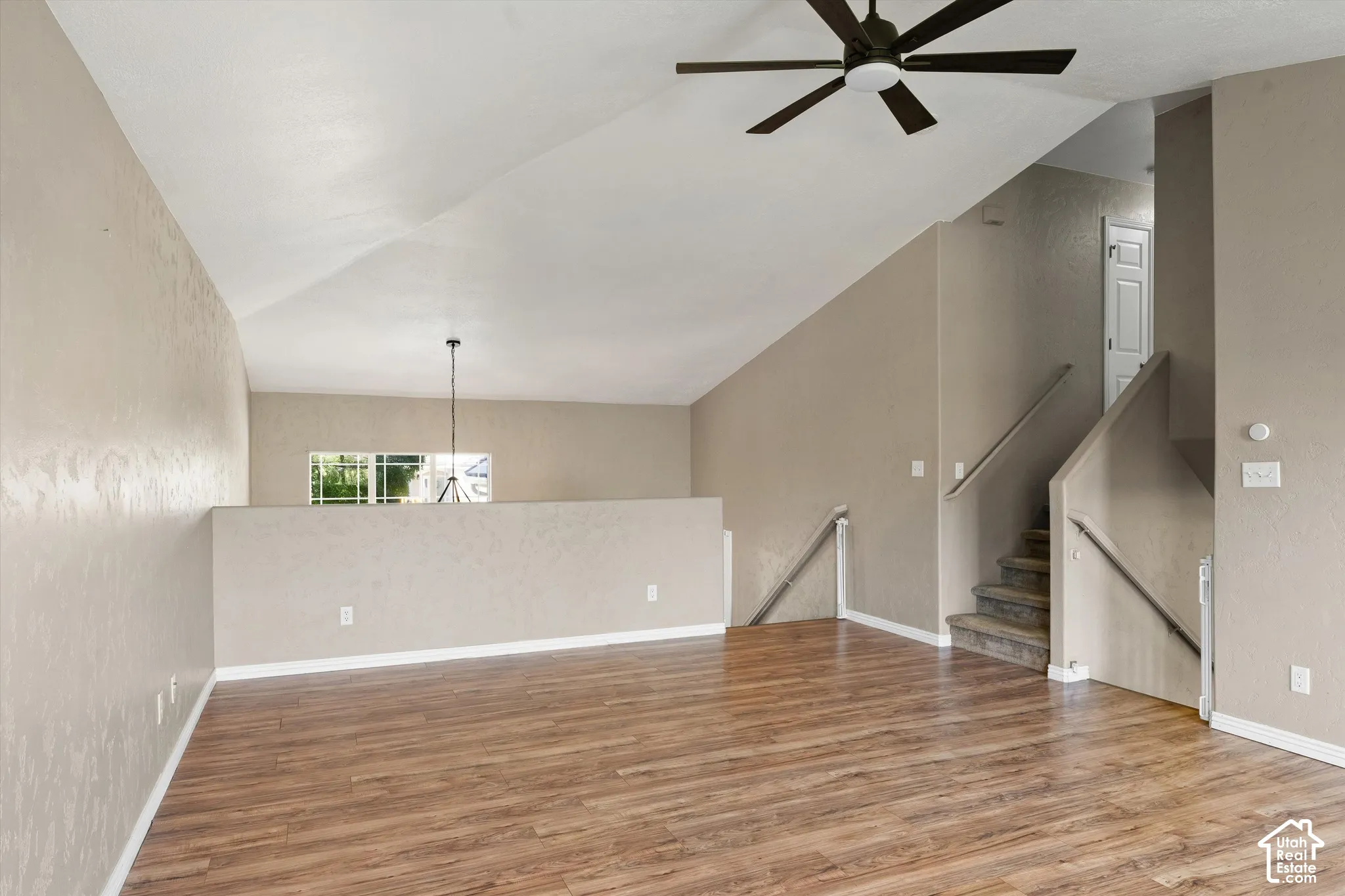 Vaulted ceiling, wood-finish flooring, ceiling fan, staircase with handrail, and interior window