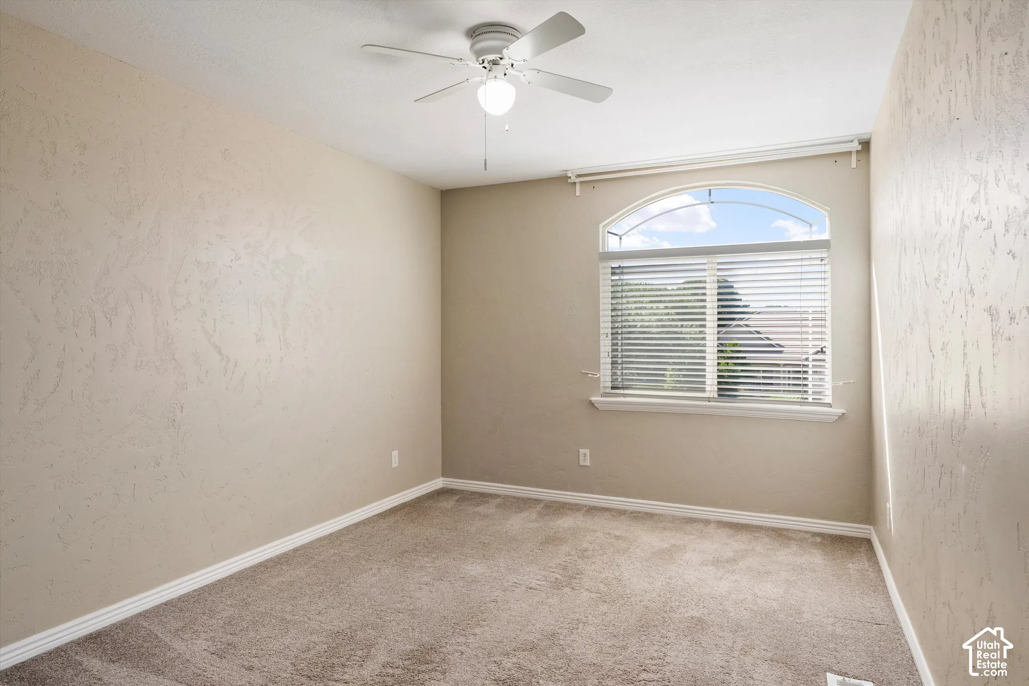 Arch-top window with blinds, ceiling fan, and textured wall finish
