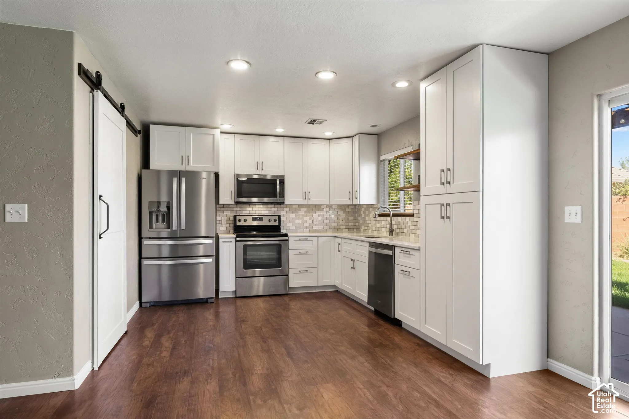 Kitchen featuring wood-finish flooring, white cabinetry, stainless steel appliances, and a tiled backsplash