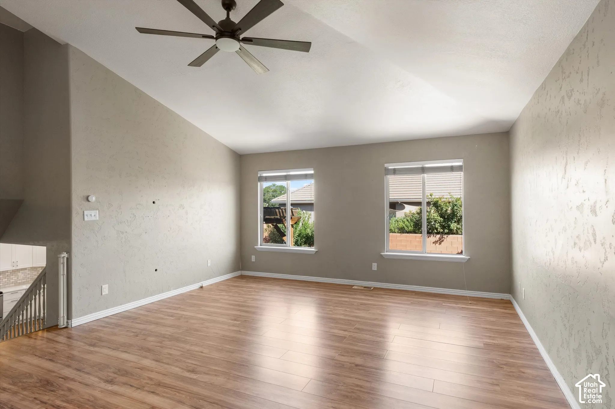 Vaulted ceiling with a ceiling fan, wood-finish flooring, and two windows