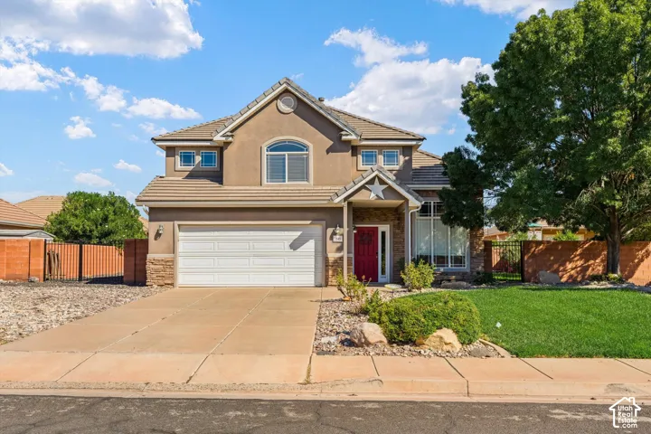 Stucco exterior with stone accents, attached two-car garage, red entry door, arched window, and mature landscaping