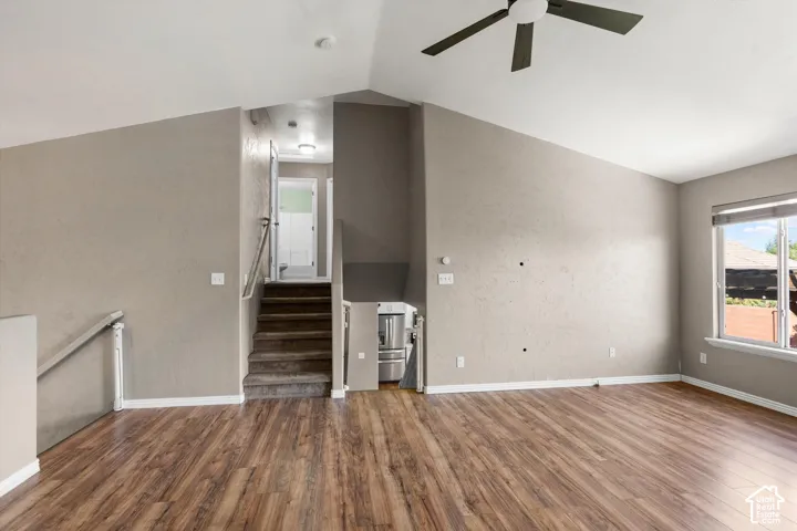 Vaulted ceiling with a ceiling fan, wood-finish flooring, staircase with carpeted treads, and a window with blinds