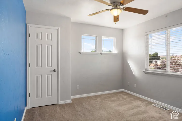 Carpeted flooring, multi-pane windows, ceiling fan with integrated lighting, and a paneled interior door