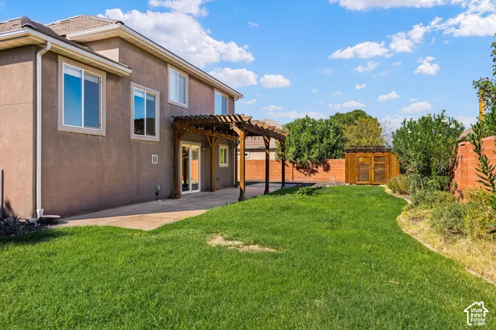 Expansive lawn with a concrete patio, wood pergola, and wood storage shed