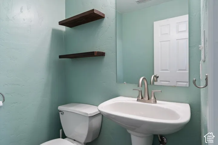 Pedestal sink with a brushed nickel faucet, wall-mounted mirror, and floating wood shelves