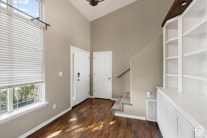 Vaulted ceiling, wood-finish flooring, built-in shelving, white trim, and a window with blinds
