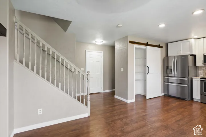 Wood-finish flooring, white spindle staircase, white paneled interior door, white kitchen cabinetry, and stainless steel refrigerator