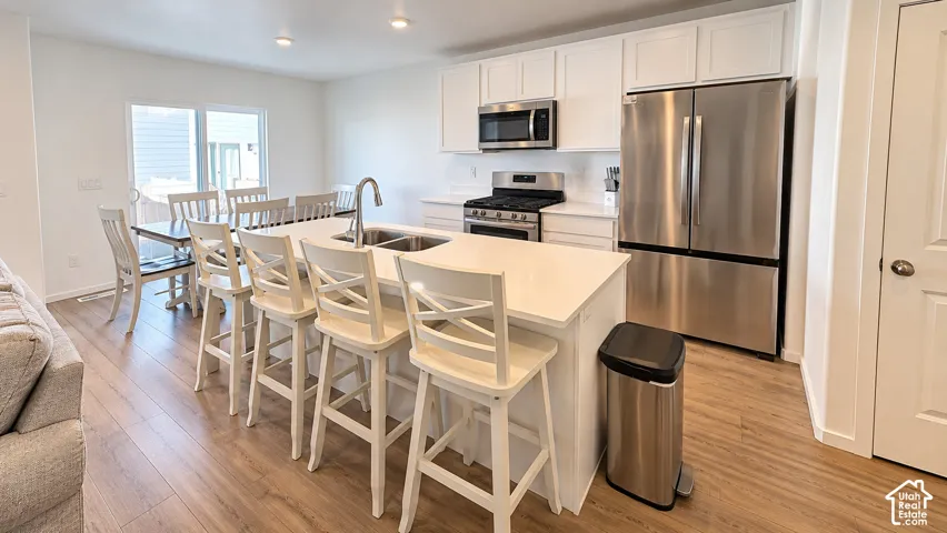 Modern kitchen featuring an island with integrated sink, white cabinetry, stainless steel appliances, and wood-finish flooring