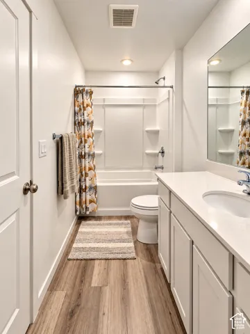 Full bathtub with shower, single vanity with white countertop, integrated sink, wood-finish flooring, and white cabinetry