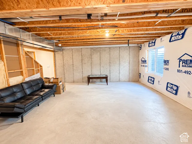 Unfinished basement featuring exposed wood joists, concrete walls, and a visible window well