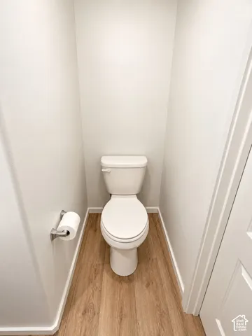 White toilet in a dedicated water closet with wood-finish flooring and a brushed nickel toilet paper holder