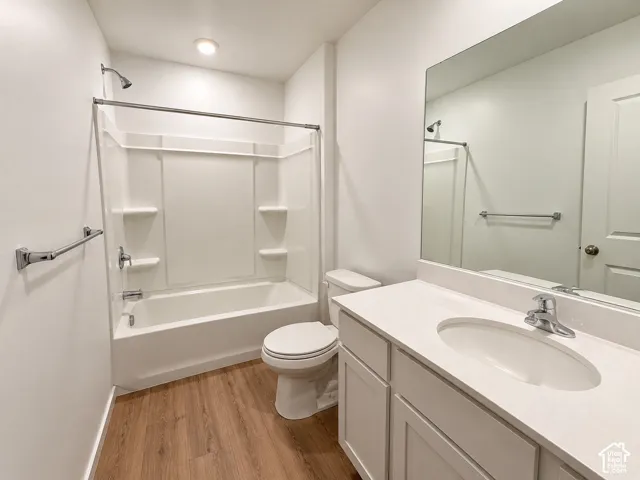 White vanity with integrated sink and chrome faucet, large frameless mirror, white bathtub with shower, and wood-finish flooring