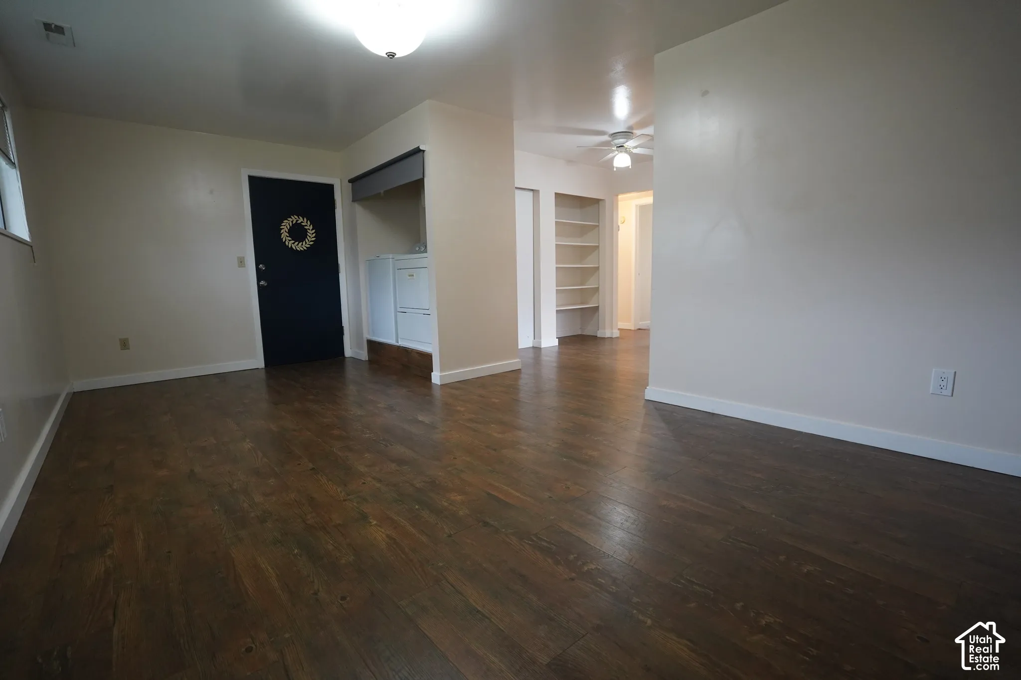 Wood-finish flooring throughout, with a built-in shelving unit, and a ceiling fan in the background