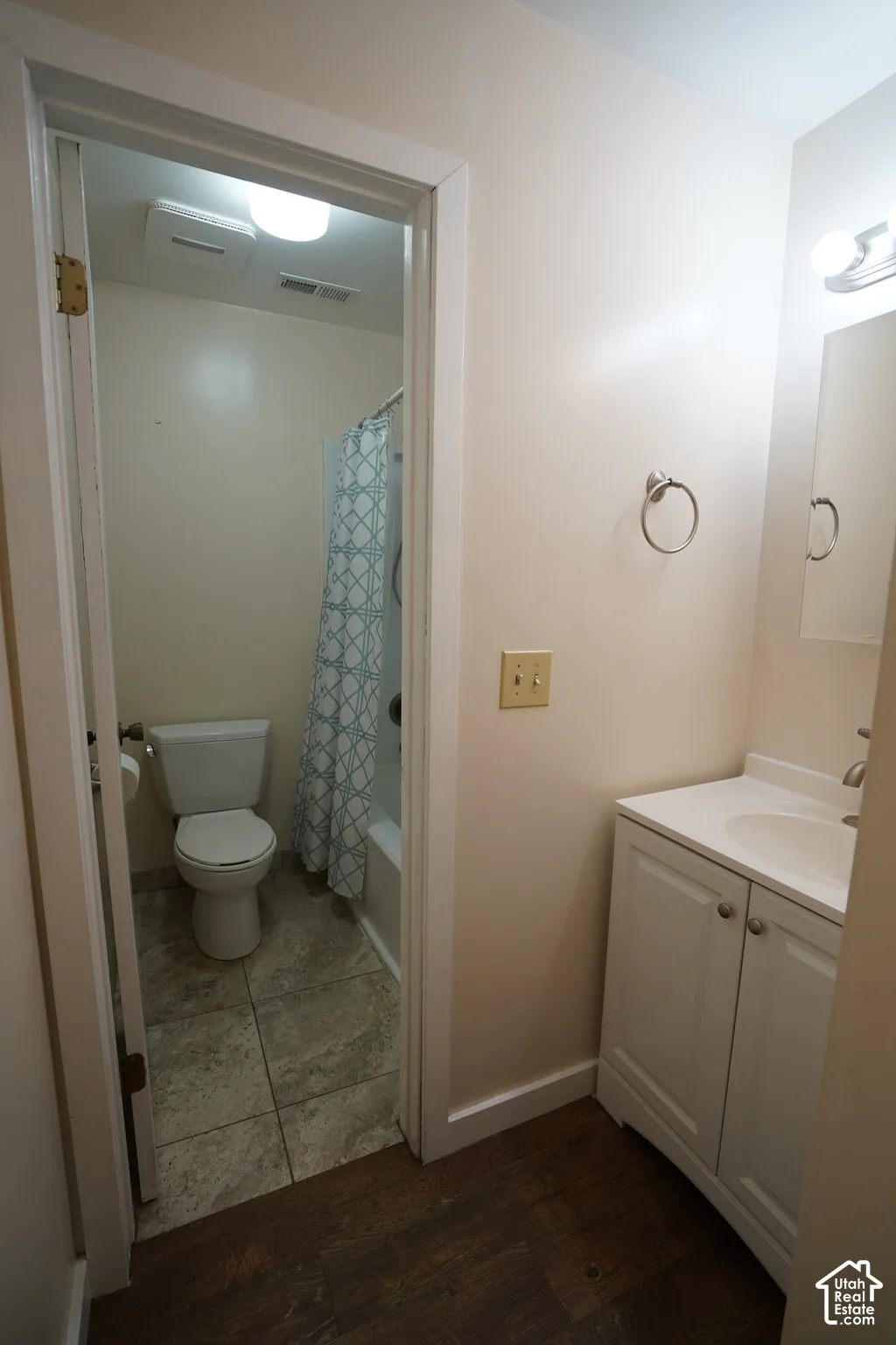 White vanity with integrated sink, wood-finish flooring, and a full bathroom with tile flooring