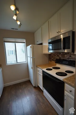 Wood-finish flooring, white cabinetry, granite-style countertops, stainless steel microwave, and tile backsplash