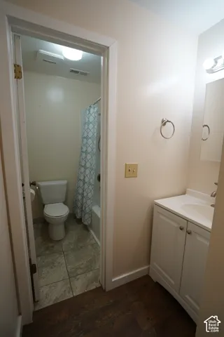 White vanity with integrated sink, wood-finish flooring, and a full bathroom with tile flooring
