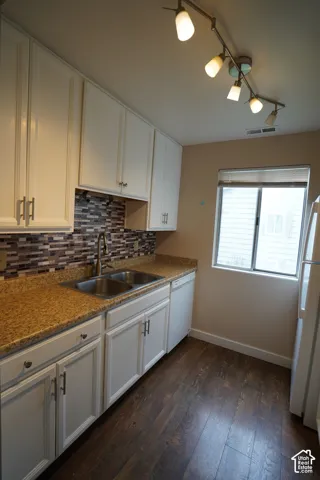White cabinetry, mosaic tile backsplash, double basin stainless steel sink, track lighting, and wood-finish flooring