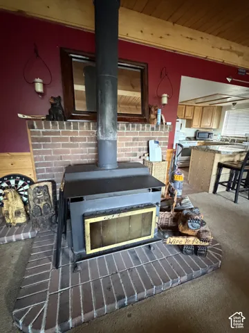 Wood-burning stove set on a brick hearth, featuring a red accent wall and exposed wood beam ceiling