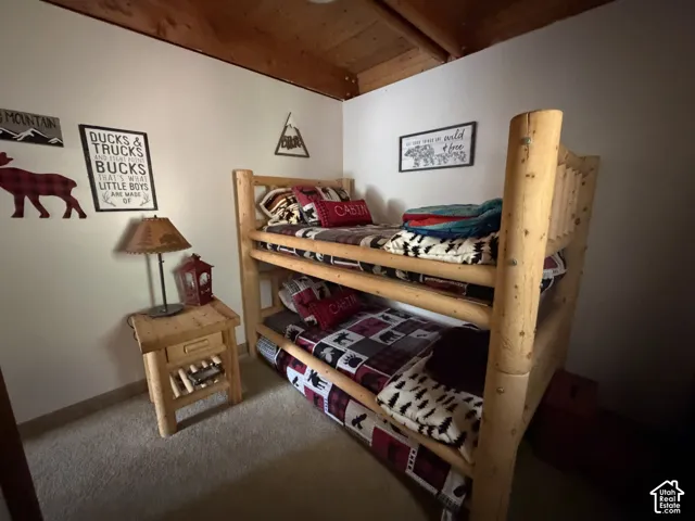Wood-finish bunk beds with natural texture, wood-finish side table with drawer, exposed wood ceiling beams, and light-toned wall finishes